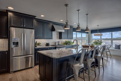 Eat-in kitchen - l-shaped light wood floor and beige floor eat-in kitchen idea in Denver with a farmhouse sink, recessed-panel cabinets, white backsplash, subway tile backsplash, stainless steel appliances, an island, granite countertops and black cabinets