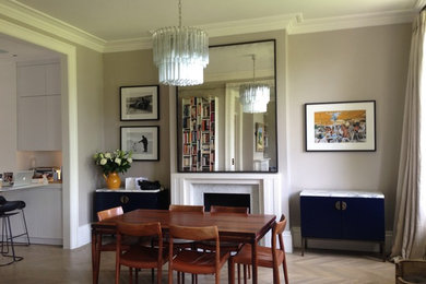 Photo of a large midcentury open plan dining room in London with beige walls, light hardwood flooring, a standard fireplace, a stone fireplace surround and beige floors.
