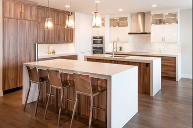 Inspiration for a huge modern l-shaped medium tone wood floor and brown floor open concept kitchen remodel in Edmonton with flat-panel cabinets, medium tone wood cabinets, solid surface countertops, white backsplash, subway tile backsplash, two islands, an undermount sink and paneled appliances