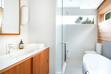 Design ideas for a mid-sized midcentury master bathroom in Vancouver with flat-panel cabinets, medium wood cabinets, engineered quartz benchtops, a freestanding tub, a two-piece toilet, white tile, porcelain tile, white walls, porcelain floors, an undermount sink and an alcove shower.