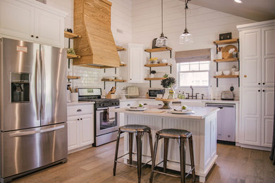 Mid-sized farmhouse l-shaped medium tone wood floor and brown floor kitchen photo in Oklahoma City with raised-panel cabinets, white cabinets, an island, a farmhouse sink, quartz countertops, white backsplash, subway tile backsplash, stainless steel appliances and white countertops