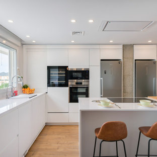 Ejemplo de cocinas en L contemporánea, grande, abierta, con fregadero bajoencimera, armarios con paneles lisos, puertas de armario blancas, encimera de cuarzo compacto, salpicadero blanco, puertas de cuarzo sintético, electrodomésticos de acero inoxidable, suelo de madera en tonos medios, una isla, suelo marrón y encimeras blancas