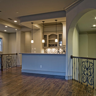 ダラスの中サイズの地中海スタイルのおしゃれな着席型バー (アンダーカウンターシンク、ガラス扉のキャビネット、グレーのキャビネット、ライムストーンカウンター、ベージュキッチンパネル、ライムストーンの床、濃色無垢フローリング、茶色い床、茶色いキッチンカウンター) の写真