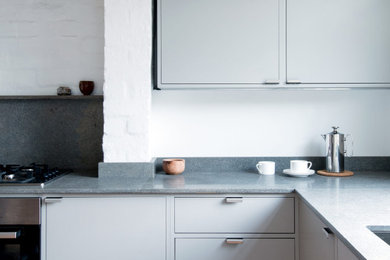 This is an example of a small contemporary l-shaped kitchen/diner in London with a double-bowl sink, flat-panel cabinets, grey cabinets, limestone worktops, grey splashback, limestone splashback, stainless steel appliances, cork flooring, no island, grey worktops and a chimney breast.