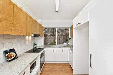 Mid-sized contemporary galley separate kitchen in Sydney with a double-bowl sink, flat-panel cabinets, white cabinets, quartz benchtops, white splashback, subway tile splashback, stainless steel appliances, medium hardwood floors, no island, brown floor and grey benchtop.