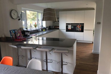 Photo of a medium sized modern u-shaped kitchen/diner in Hampshire with a submerged sink, flat-panel cabinets, white cabinets, quartz worktops, stainless steel appliances, dark hardwood flooring, brown floors and brown worktops.