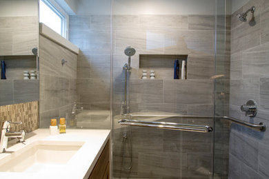 Photo of a small transitional master bathroom in Philadelphia with recessed-panel cabinets, medium wood cabinets, a curbless shower, a one-piece toilet, gray tile, porcelain tile, grey walls, porcelain floors, an undermount sink, engineered quartz benchtops, grey floor, a hinged shower door and white benchtops.