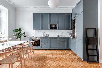 Photo of a mid-sized scandinavian l-shaped eat-in kitchen in Stockholm with blue cabinets, marble splashback, no island, an undermount sink, shaker cabinets, white splashback, stainless steel appliances and light hardwood floors.
