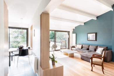 Mittelgroßes, Offenes Nordisches Wohnzimmer mit blauer Wandfarbe, hellem Holzboden, Kamin, freistehendem TV und freigelegten Dachbalken in Lyon