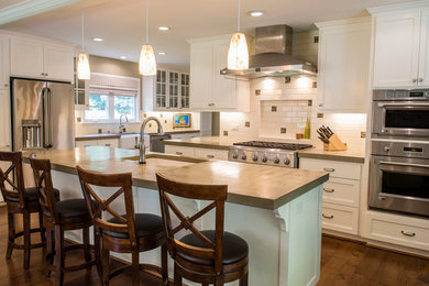 This is an example of a large transitional l-shaped open plan kitchen in San Francisco with a farmhouse sink, shaker cabinets, white cabinets, concrete benchtops, white splashback, ceramic splashback, stainless steel appliances, dark hardwood floors and with island.