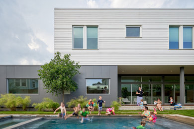This is an example of a mid-sized contemporary two-storey white house exterior in Houston with concrete fiberboard siding, a flat roof and clapboard siding.