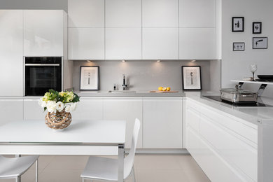 Mid-sized contemporary l-shaped eat-in kitchen in Other with quartz benchtops, grey splashback, stone slab splashback, no island, black appliances, an undermount sink, flat-panel cabinets, white cabinets and beige floor.