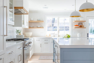Eat-in kitchen - large coastal l-shaped light wood floor and beige floor eat-in kitchen idea in Other with a farmhouse sink, shaker cabinets, white cabinets, quartz countertops, white backsplash, subway tile backsplash, stainless steel appliances, an island and white countertops