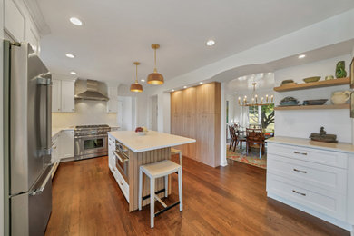 Kitchen - contemporary u-shaped medium tone wood floor and brown floor kitchen idea in New York with recessed-panel cabinets, white cabinets, quartz countertops, white backsplash, quartz backsplash, stainless steel appliances, an island and white countertops