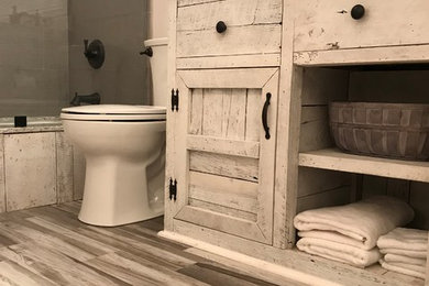 This is an example of a large beach style master bathroom in Other with shaker cabinets, distressed cabinets, an alcove tub, a shower/bathtub combo, a two-piece toilet, gray tile, porcelain tile, beige walls, laminate floors, an undermount sink, quartzite benchtops, beige floor, an open shower and beige benchtops.