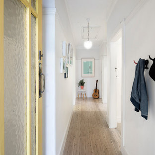 Inredning av en eklektisk entré, med vita väggar, ljust trägolv, en enkeldörr och en gul dörr