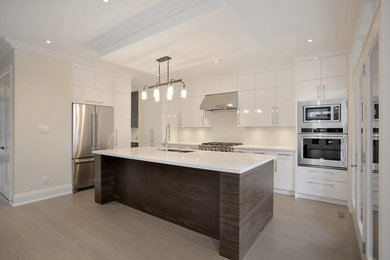 Large trendy u-shaped light wood floor and brown floor enclosed kitchen photo in Toronto with a double-bowl sink, white cabinets, quartz countertops, white backsplash, stainless steel appliances, an island, flat-panel cabinets and glass tile backsplash