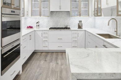 Inspiration for a contemporary brown floor and laminate floor kitchen remodel in Los Angeles with an undermount sink, glass-front cabinets, white cabinets, marble countertops, white backsplash, stone slab backsplash, stainless steel appliances and white countertops