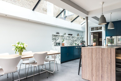 Large modern galley eat-in kitchen in London with a drop-in sink, flat-panel cabinets, blue cabinets, marble benchtops, grey splashback, marble splashback, stainless steel appliances, concrete floors and with island.