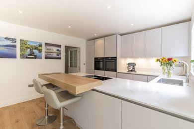 Design ideas for a medium sized modern u-shaped kitchen/diner in Hampshire with an integrated sink, flat-panel cabinets, grey cabinets, quartz worktops, integrated appliances, medium hardwood flooring, a breakfast bar, white worktops and feature lighting.