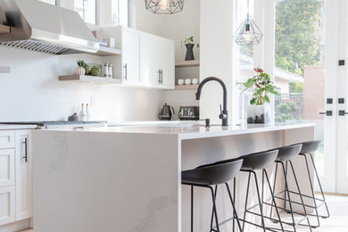 Scandinavian l-shaped kitchen in Vancouver with an undermount sink, shaker cabinets, white cabinets, quartz benchtops, white splashback, stainless steel appliances, light hardwood floors, with island and white benchtop.