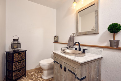 Mid-sized mountain style multicolored floor powder room photo in Other with flat-panel cabinets, light wood cabinets, a two-piece toilet, white walls, a drop-in sink, marble countertops and gray countertops
