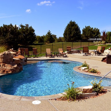 Free form pool with stone table, sun shelf, water feature, and outdoor kitchen,