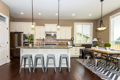 Large transitional single-wall medium tone wood floor open concept kitchen photo in Portland with an undermount sink, recessed-panel cabinets, white cabinets, granite countertops, beige backsplash, ceramic backsplash, stainless steel appliances and an island