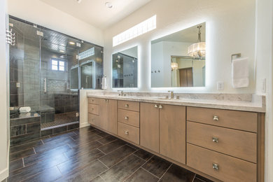 This is an example of a large modern master bathroom in Phoenix with flat-panel cabinets, medium wood cabinets, a double shower, a one-piece toilet, gray tile, porcelain tile, beige walls, porcelain floors, an undermount sink, engineered quartz benchtops, grey floor, a hinged shower door and grey benchtops.