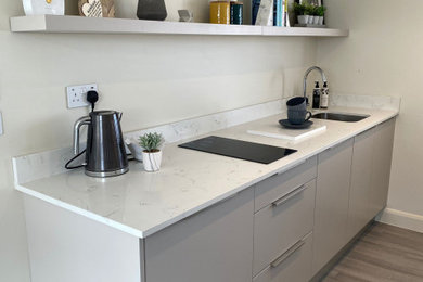 This is an example of a medium sized modern galley kitchen/diner in London with a single-bowl sink, flat-panel cabinets, quartz worktops, black appliances, vinyl flooring, grey floors and white worktops.