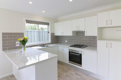 Photo of a small contemporary u-shaped open plan kitchen in Central Coast with a single-bowl sink, white cabinets, laminate benchtops, grey splashback, ceramic splashback, stainless steel appliances, light hardwood floors and no island.