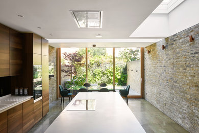 Inspiration for a mid-sized modern single-wall eat-in kitchen in London with an integrated sink, flat-panel cabinets, solid surface benchtops, metallic splashback, mirror splashback, stainless steel appliances, concrete floors, with island, grey floor, white benchtop and medium wood cabinets.