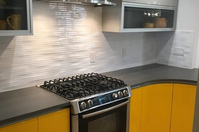 Example of a mid-sized trendy u-shaped light wood floor and beige floor enclosed kitchen design in San Francisco with no island, an undermount sink, flat-panel cabinets, yellow cabinets, quartz countertops, white backsplash, ceramic backsplash, stainless steel appliances and black countertops