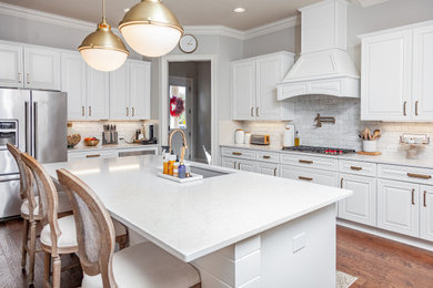 This is an example of a large contemporary eat-in kitchen in Atlanta with a single-bowl sink, raised-panel cabinets, white cabinets, quartz benchtops, grey splashback, marble splashback, stainless steel appliances, medium hardwood floors, with island, brown floor and white benchtop.
