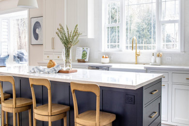 Eat-in kitchen - large coastal l-shaped medium tone wood floor and brown floor eat-in kitchen idea in Philadelphia with a farmhouse sink, recessed-panel cabinets, blue cabinets, quartzite countertops, white backsplash, ceramic backsplash, stainless steel appliances, an island and white countertops