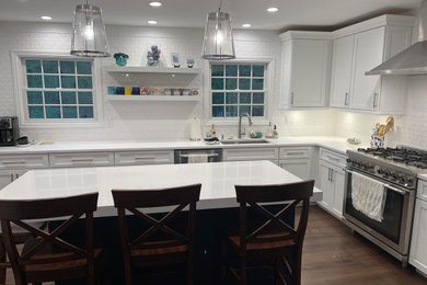 Inspiration for a large transitional l-shaped medium tone wood floor and brown floor eat-in kitchen remodel in New York with an undermount sink, recessed-panel cabinets, blue cabinets, quartz countertops, white backsplash, ceramic backsplash, stainless steel appliances, an island and white countertops