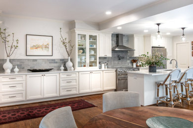 Inspiration for a mid-sized timeless single-wall medium tone wood floor and multicolored floor eat-in kitchen remodel in Houston with a drop-in sink, shaker cabinets, white cabinets, quartz countertops, gray backsplash, stone tile backsplash, stainless steel appliances, an island and white countertops