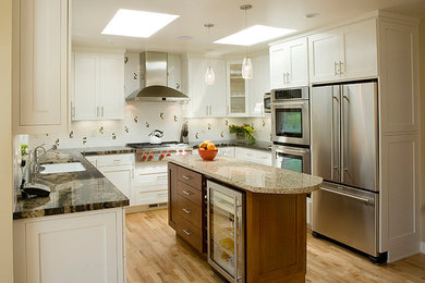 Photo of a traditional u-shaped eat-in kitchen in San Francisco with raised-panel cabinets, white cabinets, granite benchtops, white splashback, stainless steel appliances, light hardwood floors and with island.