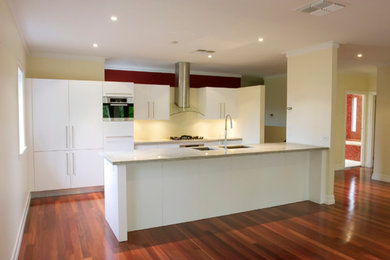 Mid-sized modern single-wall eat-in kitchen in Brisbane with an undermount sink, white cabinets, white splashback, stainless steel appliances, medium hardwood floors and with island.