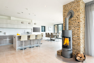 This is an example of an expansive modern open concept living room in Gloucestershire with green walls, porcelain floors, a wood stove, a stone fireplace surround, a built-in media wall and brown floor.