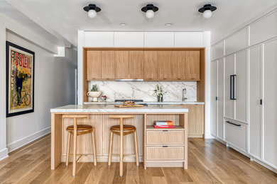 Example of a trendy l-shaped medium tone wood floor and brown floor kitchen design in New York with an undermount sink, shaker cabinets, medium tone wood cabinets, white backsplash, stone slab backsplash, paneled appliances, an island and white countertops