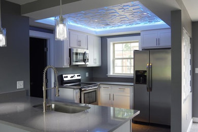 Example of a mid-sized minimalist l-shaped medium tone wood floor and brown floor kitchen design in Other with shaker cabinets, white cabinets, quartzite countertops, gray backsplash, stainless steel appliances and a peninsula