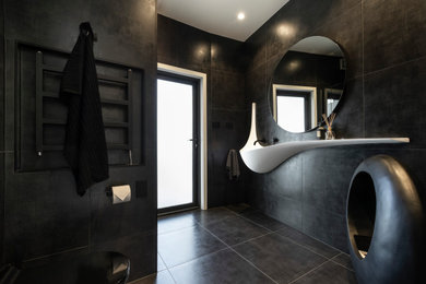 Mid-sized modern 3/4 bathroom in Auckland with white cabinets, a corner shower, black tile, ceramic tile, black walls, ceramic floors, a wall-mount sink, engineered quartz benchtops, black floor, a hinged shower door, white benchtops, a single vanity, a floating vanity and a wall-mount toilet.