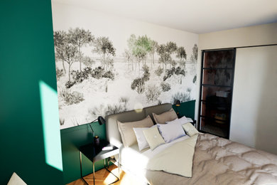 Aménagement d'une grande chambre parentale industrielle avec un mur vert, parquet clair, du papier peint et verrière.