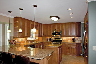 Inspiration for a mid-sized timeless u-shaped ceramic tile and beige floor enclosed kitchen remodel in New York with a double-bowl sink, raised-panel cabinets, medium tone wood cabinets, granite countertops, beige backsplash, ceramic backsplash, stainless steel appliances and an island