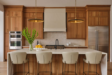 Inspiration for a large transitional medium tone wood floor kitchen remodel in Other with a farmhouse sink, medium tone wood cabinets, quartzite countertops, white backsplash, stainless steel appliances, an island and white countertops