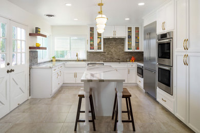 Inspiration for a mid-sized transitional u-shaped porcelain tile and beige floor open concept kitchen remodel in Los Angeles with a single-bowl sink, recessed-panel cabinets, white cabinets, quartz countertops, brown backsplash, stone tile backsplash, stainless steel appliances, an island and white countertops