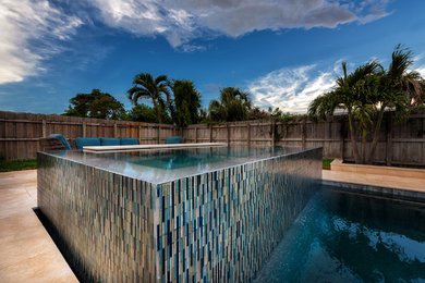 Inspiration for a mid-sized modern backyard custom-shaped infinity pool in Miami with a hot tub and natural stone pavers.