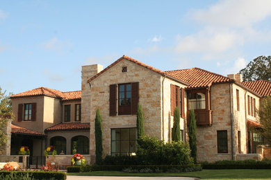 This is an example of a large mediterranean two-storey beige house exterior in Dallas with stone veneer, a hip roof and a tile roof.