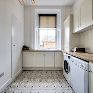 グラスゴーの大きいトランジショナルスタイルのおしゃれな洗濯室 (一体型シンク、シェーカースタイル扉のキャビネット、ベージュのキャビネット、木材カウンター、ベージュの壁、左右配置の洗濯機・乾燥機、マルチカラーの床、茶色いキッチンカウンター) の写真